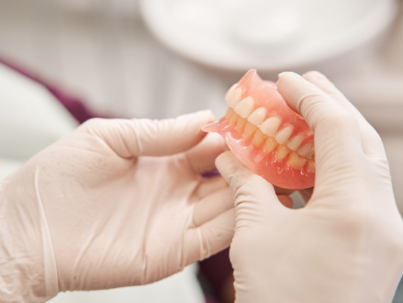 White-gloved hands holding complete set of dentures