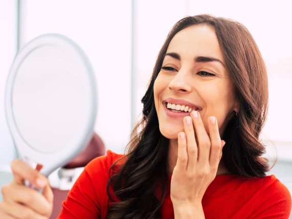 A woman admiring her new dental implants in a hand mirror